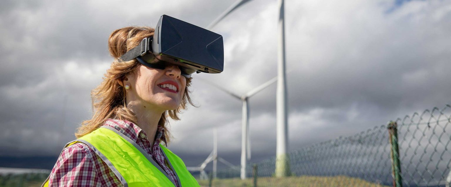 Frau mit VR-Brille vor Windpark bei bewölktem Himmel.
