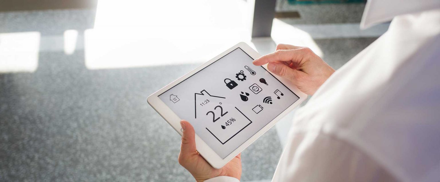 Person hält Tablet mit Smart-Home-Steuerung; angezeigt: 22 °C, 45 % Luftfeuchtigkeit und anderes.