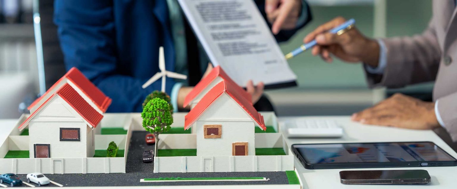 Zwei Personen mit Dokument an Tisch mit Modell, Windrad und Tablet.