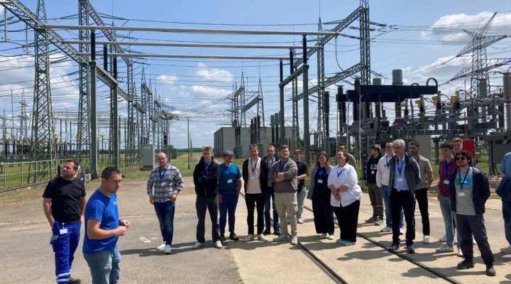 Führung durch Umspannanlage mit Hochspannungsleitungen; Gruppe hört zu.
