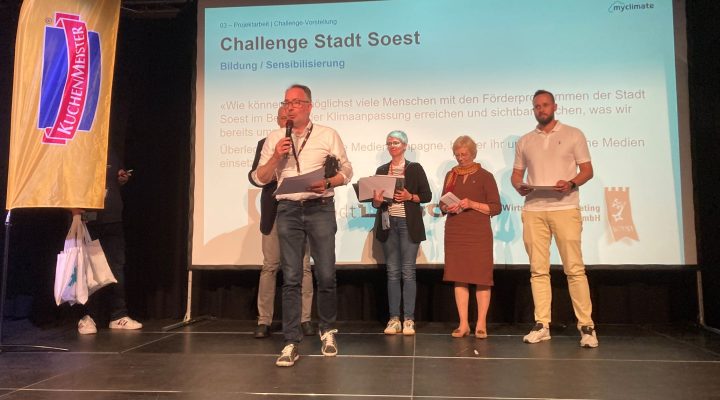 Fünf Personen auf Bühne vor ‚Challenge Stadt Soest‘-Bildschirm; links ‚Kuchenmeister‘-Fahne.